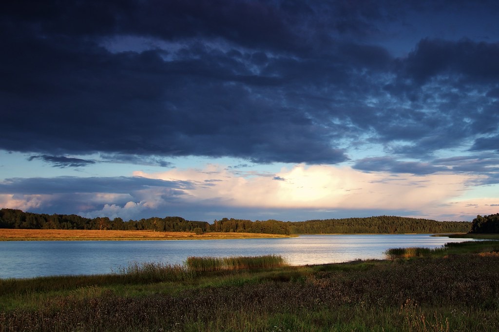 First light breaking through clearing clouds over still water at dawn, a calm morning landscape.